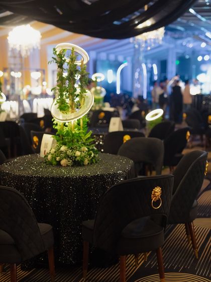Chic cocktail tables with black sequined tablecloths and modern, illuminated centerpieces. The chairs feature a unique gold lion-head accent, adding a touch of luxury.