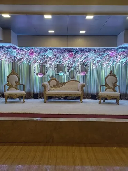 A beautiful stage at Devanshi Inn Hotel & Banquets. The backdrop is covered in purple and blue flowers, creating a rich and colorful setting for a wedding or reception.