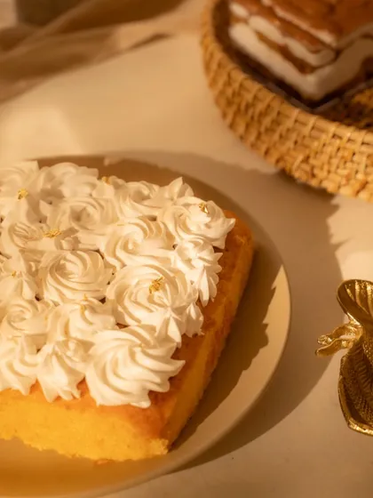 A slice of fluffy cake with meringue frosting, captured in soft, natural light. The gold leaf details add a touch of elegance to this simple and beautiful dessert photo.