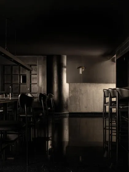The main bar area, characterized by its brutalist black concrete and polished black floors. The reflections create a sense of depth and movement in the otherwise still and silent space.