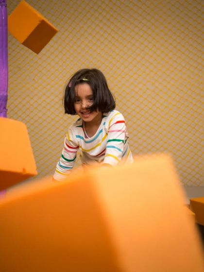 A happy face emerges from a flurry of flying foam blocks. The foam pit is a zone of endless, energetic fun.