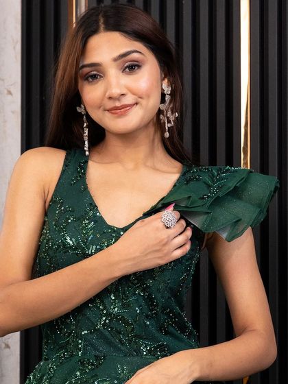 A close-up of the emerald green gown, highlighting the sequin work and the delicate ruffle on the shoulder.