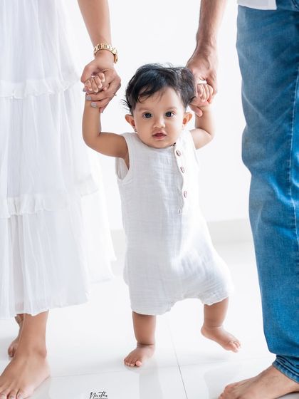 A baby taking her first steps with her parents' help.