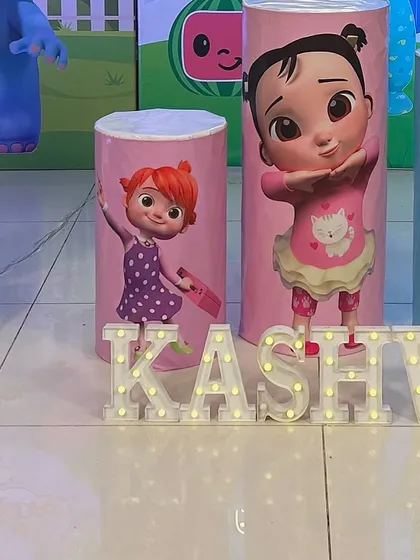 A close-up of the personalized details for a Cocomelon party, including themed pedestals and light-up marquee letters for the name 'Kashvi'.