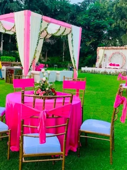 An outdoor seating arrangement for a pink-themed day wedding. The bright pink table cloths and chair ties stand out beautifully against the green lawn.