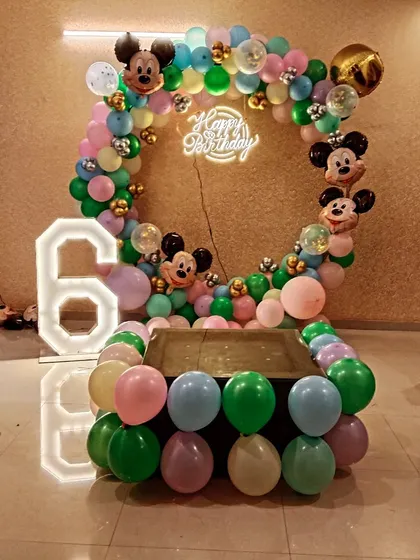 A Mickey Mouse themed 6th birthday party. The circular balloon arrangement is decorated with Mickey Mouse foil balloons and surrounds a central table, with a large light-up number '6' on the side.