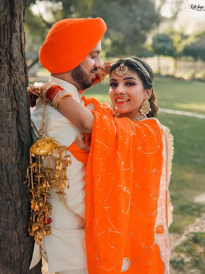 This pre-wedding photo captures the bride's playful side as she embraces her groom. The focus is on her beautiful smile and the intricate details of her kalire against the natural backdrop.