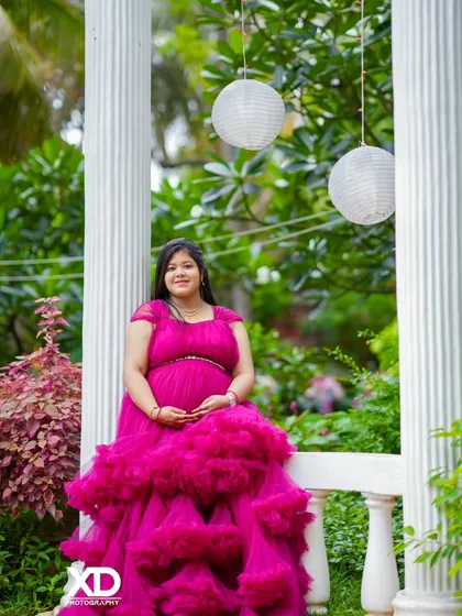 A lovely solo portrait of the mother-to-be seated on a white bench in a lush garden.