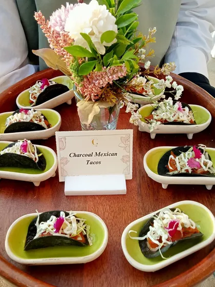 Our Charcoal Mexican Tacos are a modern marvel. Served on a tray with a floral arrangement, these visually striking tacos are filled with deliciousness and topped with fresh slaw.