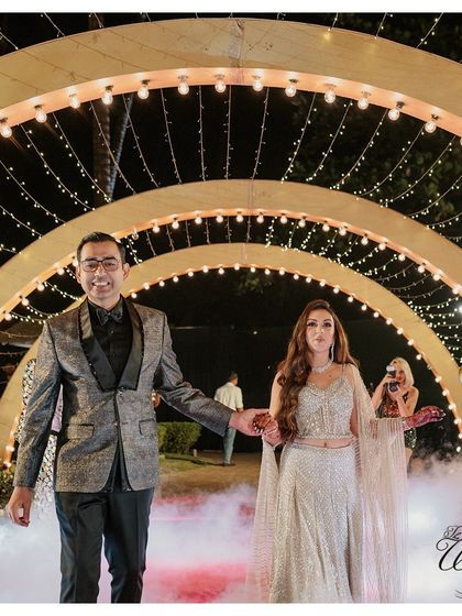 A beautiful shot of the couple making their entrance through an archway of warm lights, with fog effects adding to the dreamy and dramatic atmosphere.
