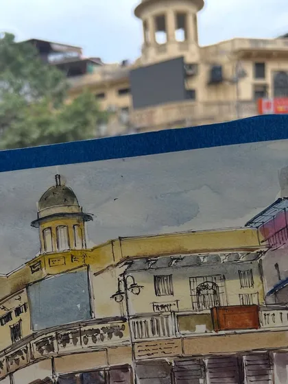 My sketchbook in action at Chandni Chowk. This view shows my watercolor sketch with the actual building in the background, capturing the moment of creation.