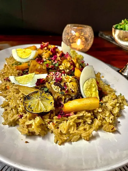 A beautifully plated Mutton Yakhni Pulao, garnished with fried lime, boiled eggs, and rose petals, showcasing an elegant presentation for a sit-down dinner.