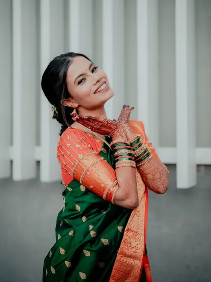 A happy bride in her green and orange saree. The makeup is subtle, with a focus on enhancing her natural features and joyful expression.