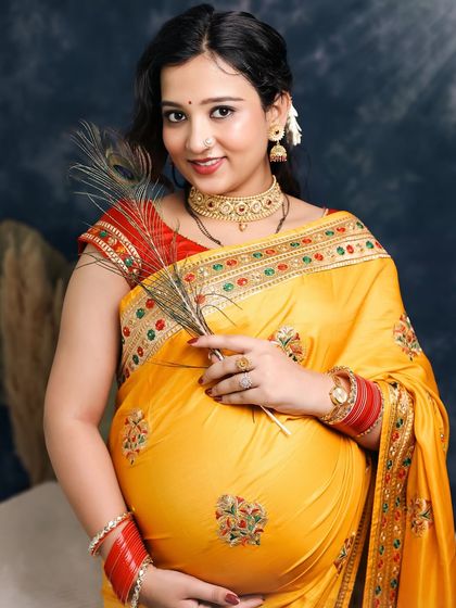 A bright and happy portrait of the mother-to-be. Holding a peacock feather, she smiles directly at the camera, her joy and traditional attire making for a beautiful and engaging image.