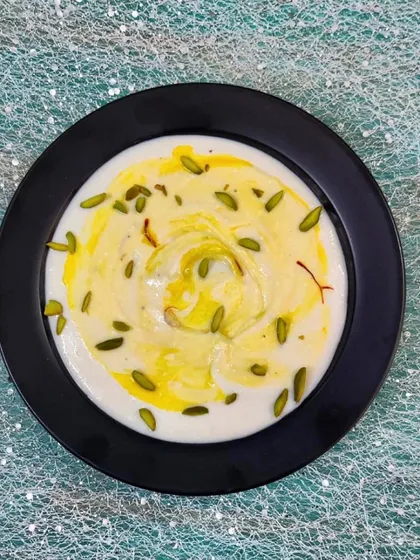 A bowl of creamy, homemade Shrikhand, garnished with saffron and pistachios. This sweet and tangy yogurt-based dessert is a perfect end to any meal, especially when paired with hot puris.