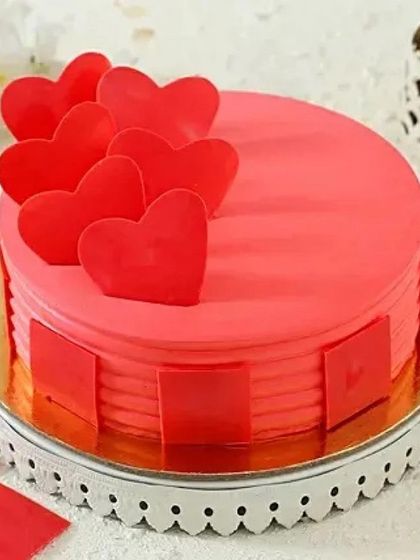 A vibrant and cheerful cake to celebrate your love. This round cake features a bright red frosting and is topped with multiple edible hearts, making it a fun and modern option for any romantic occasion.