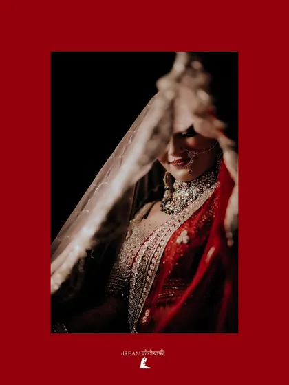 A beautiful shot of the bride Khushbu, peeking through her red dupatta, her smile and jewelry creating a captivating frame.