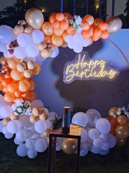 An elegant outdoor party setup with an orange and white balloon ring. I added small floral accents and a neon "Happy Birthday" sign for a touch of sophistication.