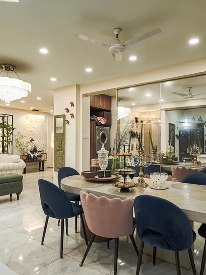 A wide shot of an open-plan home, showing the dining area with jewel-toned chairs flowing into the living room, unified by a large mirrored wall that enhances the sense of space.