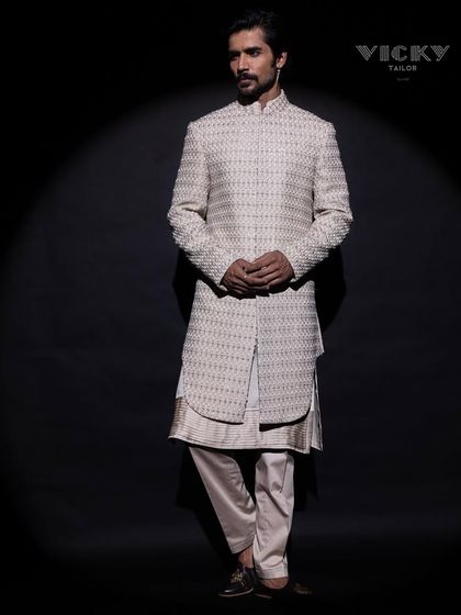 This spotlight moment highlights the sharp silhouette and intricate texture of our layered sherwani. It is a piece designed to look magnificent from every angle.