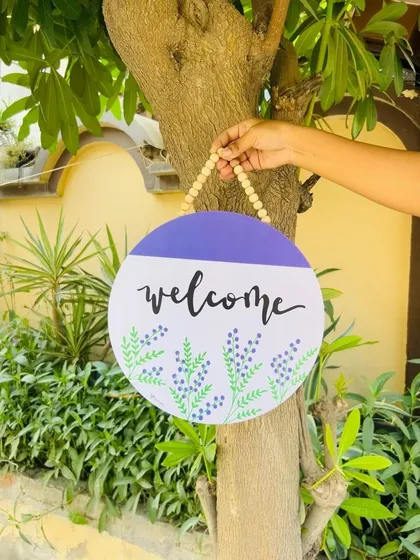Another look at our 'Welcome' wooden sign, hanging on a tree. The simple yet elegant design with hand-doodled lavender flowers makes for a charming and personal touch to your home's entrance.