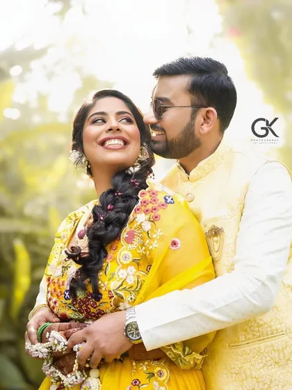 A happy couple posing in a garden, with the bride wearing a vibrant yellow lehenga and our floral jewellery.
