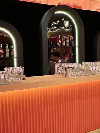 A bar should be more than just a counter; it should be a destination. For this modern cocktail party, we designed and built a sleek, illuminated bar with a fluted orange base and backlit arched shelves to create a vibrant social hub.