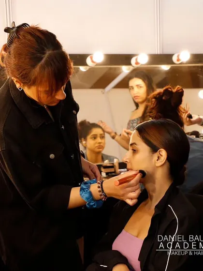 A student works on a model's base makeup in the bustling backstage environment of fashion week, gaining invaluable hands-on experience.