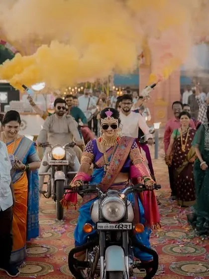 Making an entrance that nobody will forget. A cool bride in her traditional Maharashtrian attire rides in on a motorcycle, surrounded by yellow smoke and her cheering family.