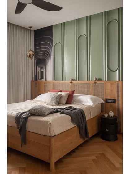The guest bedroom is defined by a serene, pastel green paneled wall with inset arches. The bed, crafted from light oak with a cane headboard, adds natural texture. This room was designed to be a calm and welcoming space for visitors.