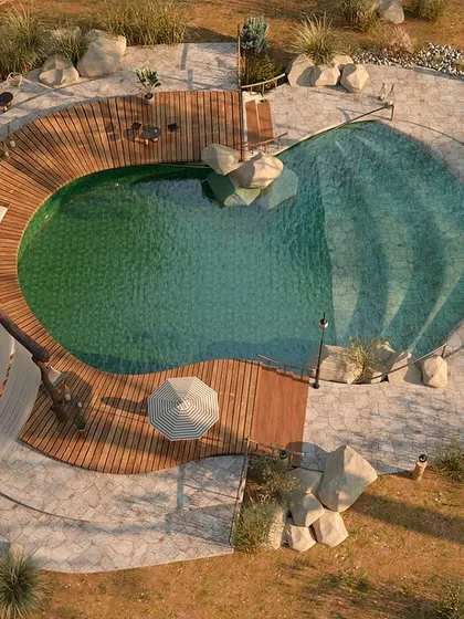 An alternate aerial view of the pool, showcasing its unique, free-form shape. The design includes both a wooden deck and stone patio areas, offering a variety of textures and spaces for guests to enjoy around the water.