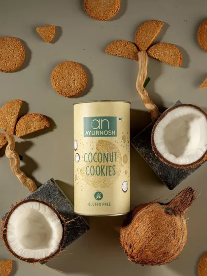 A creative flatlay for Ayurnosh's gluten-free coconut cookies. The ingredients like coconuts and cookie-made palm trees visually tell the story of the product's flavor and natural origins.