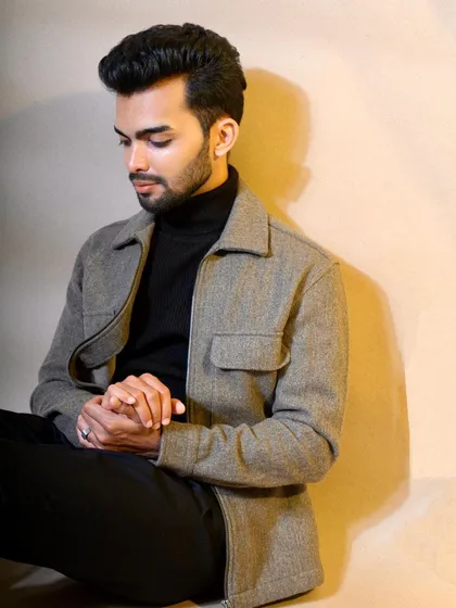 A quiet, contemplative shot of the model seated in a grey felt jacket. This image showcases the texture and fit of the jacket in a relaxed, natural pose suitable for lookbooks.