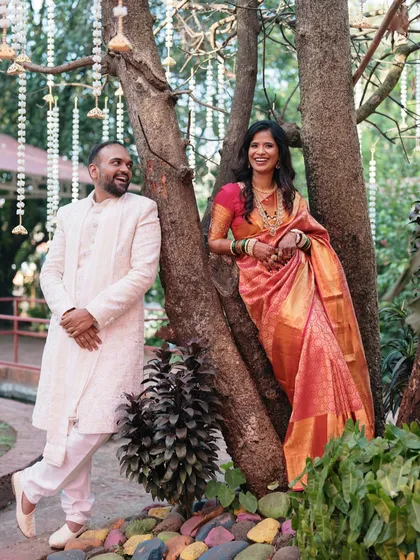 Leaning against a tree in a sunlit garden, the couple shares a candid moment. This portrait feels natural, joyful, and full of life.
