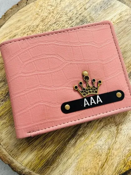 A beautiful pink croc-textured wallet, customized with a name on a black plate and a crown charm.