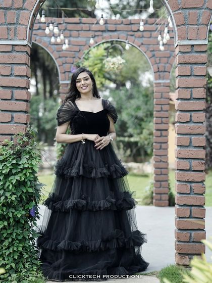 A full-length portrait of the bride-to-be in her elegant black gown, framed by a brick archway in a beautiful garden.