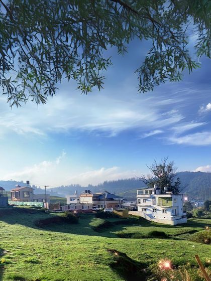 The picturesque landscape of Ooty, with its charming houses and green fields under a bright blue sky. It feels like a different world.