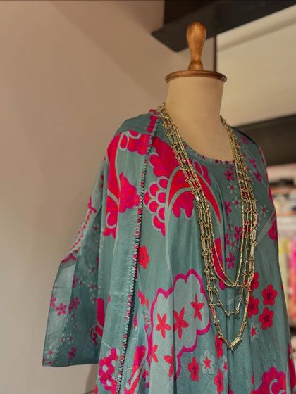 A close-up of a teal and pink floral dress, styled with a layered necklace for a bohemian touch.