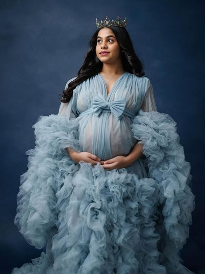 A regal and thoughtful pose, with the mother-to-be wearing a crown and a voluminous blue gown, looking towards the future.