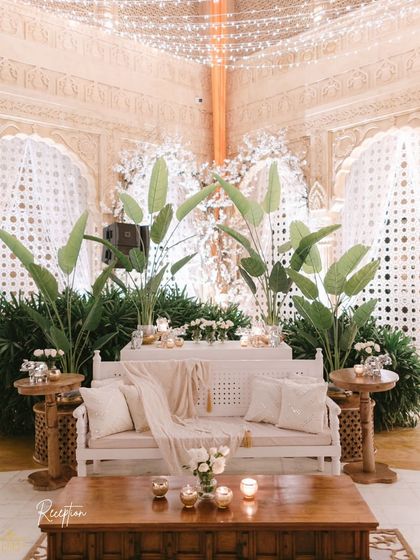 The couple's seating area at the all-white reception. A comfortable white bench was styled with lush greenery, elegant throws, and candles, creating a chic and cozy spot for the couple to relax and take in the celebration.