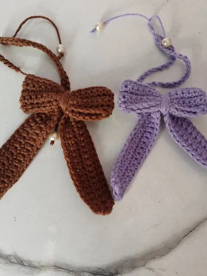 These simple yet elegant crochet bows in lavender and brown are detailed with a tiny pearl. They are perfect for adding a subtle touch of handmade charm to your hair or even as a bag accessory.