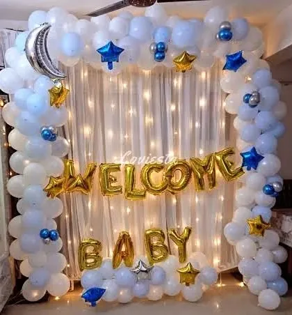 A dreamy 'Welcome Baby' decoration with a celestial theme. A white balloon arch is accented with silver moon and star foil balloons against a backdrop of fairy lights.