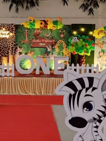 A full-stage view of a jungle safari first birthday. The design includes a lush backdrop, a variety of animal cutouts like a zebra and giraffe, and a large "ONE" sign for the perfect photo opportunity.