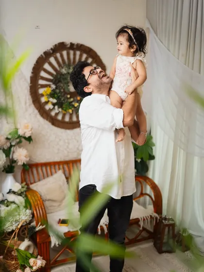 A candid shot of a father and his daughter, framed by greenery in the studio. His joyful expression as he lifts her up is a perfect example of a natural, unposed moment.