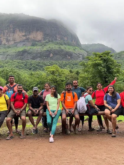 The group takes a break during a trek in Maharashtra, with a massive flat-topped mountain in the background.