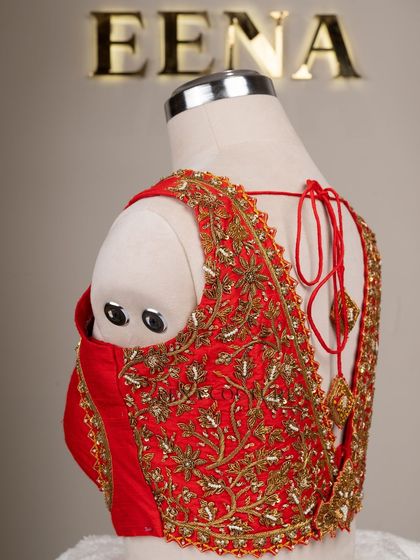 This sleeveless red blouse is perfect for a bold bridal statement. It features a deep V-neckline and is heavily embellished with intricate gold floral zardozi work, creating a rich and luxurious feel.