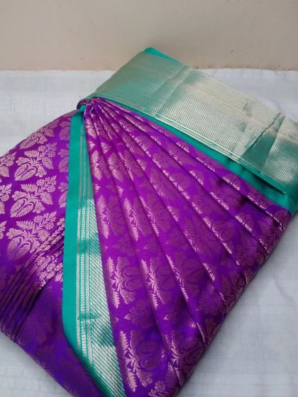 A royal purple Kanjeevaram with a teal and silver border. The pleats are sharp and defined, ready to create a stunning drape.