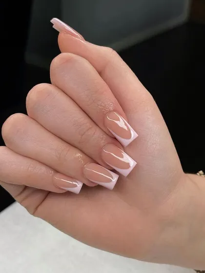 A close-up of a soft pink French manicure, showing the clean lines and glossy finish.