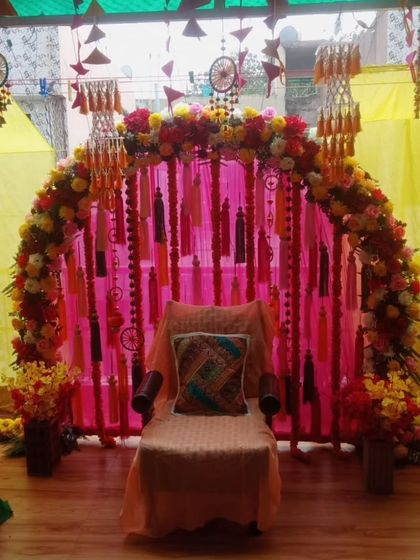 A simple and sweet seating for a home Mehandi or Haldi. The floral arch is decorated with colorful tassels and dreamcatchers, creating a charming and personal space.