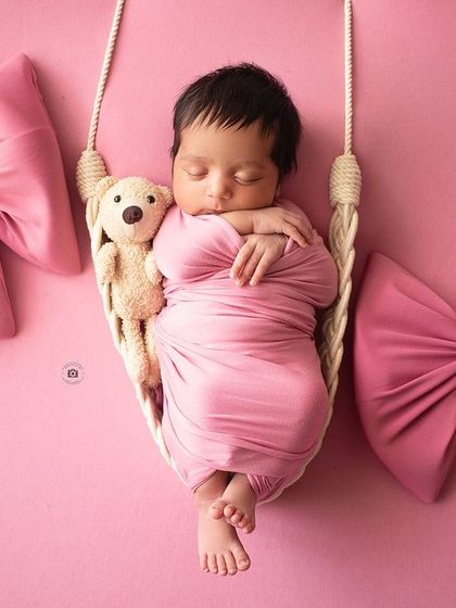 A sweet newborn sleeps on a hanging prop, flanked by two large pink bows for a cute and girly setup.